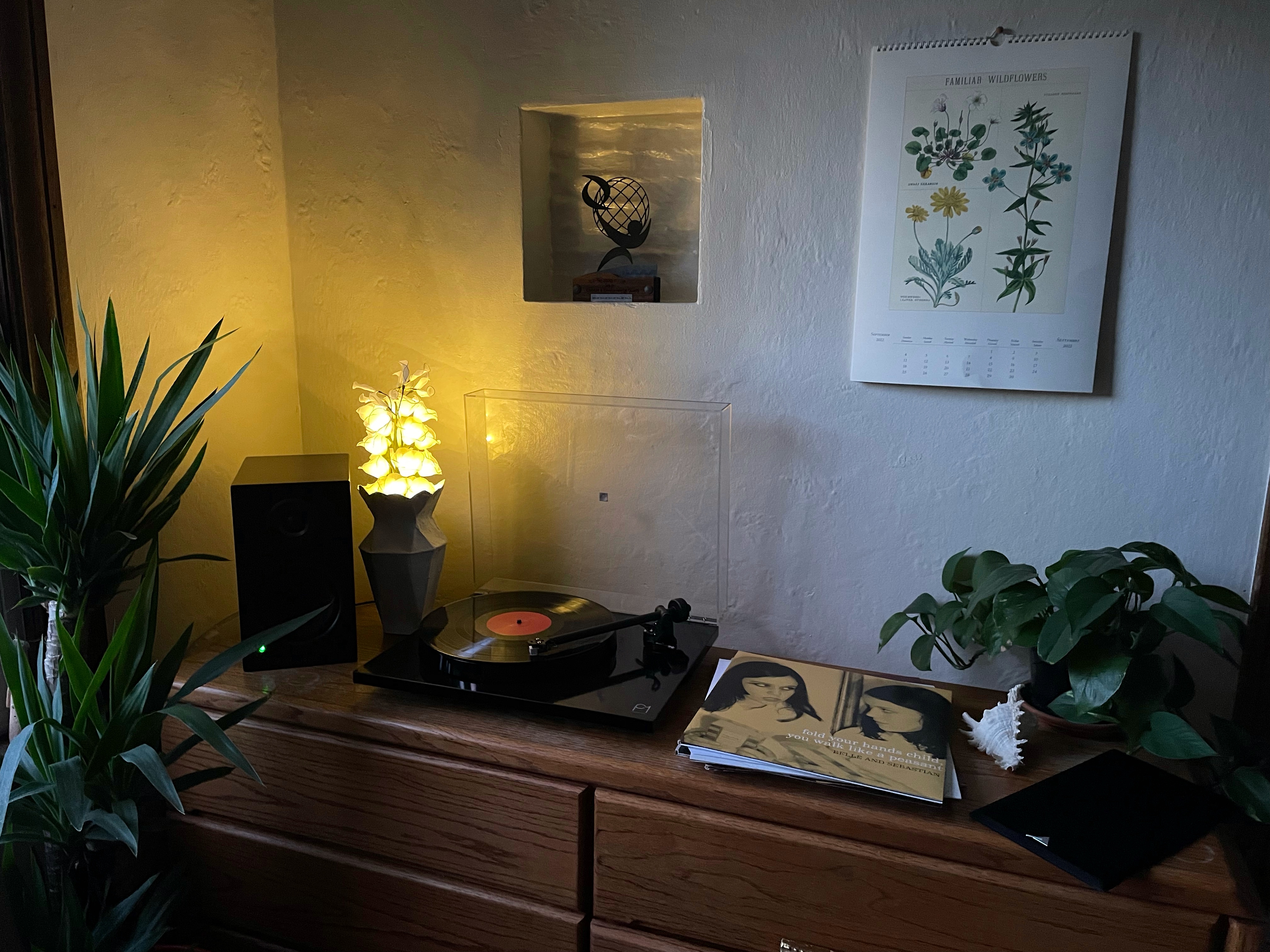 corner of my apartment where a turntable and speaker and pile of records sits on top of a dresser, there is a calendar hanging on the wall.